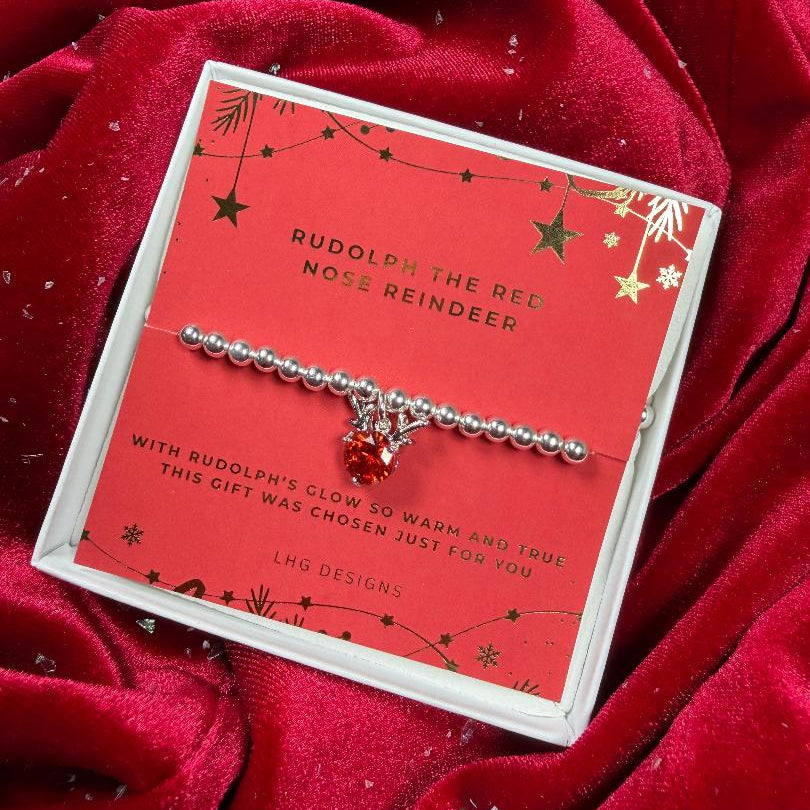 Silver bracelet with a red charm on a Rudolph-themed card against a red fabric background